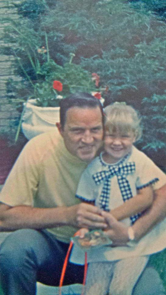 A father and his daughter share a joyful moment in a garden, smiling broadly.
