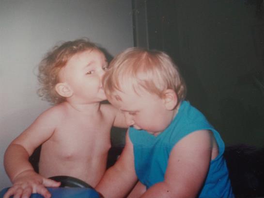 Two children engage in a playful interaction, one whispering to the other in a cozy room.