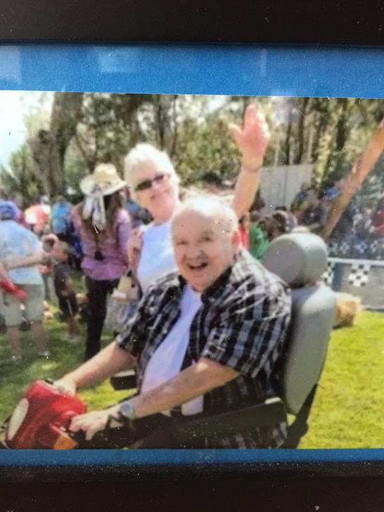 Two seniors smile and engage happily at a vibrant community festival in bright sunlight.