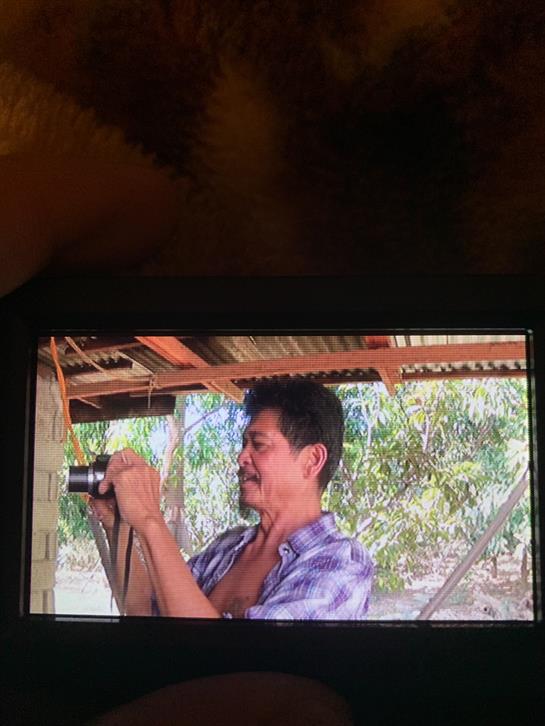A man photographs his surroundings in a rustic location filled with greenery.