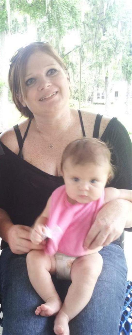 A mother holds her baby close, both wearing comfortable clothing, on a sunny afternoon.