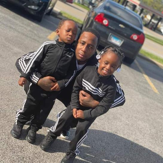 A happy father and his two kids wear matching athletic gear in a parking lot.