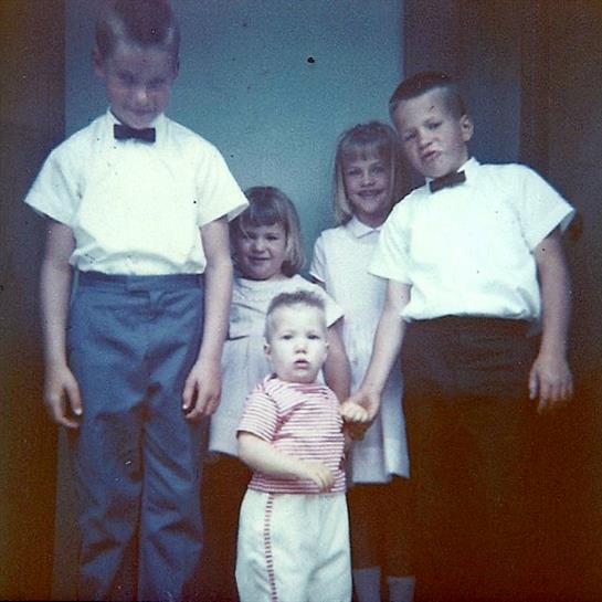 Five children stand together outside a building, dressed in formal clothing, smiling and posing.