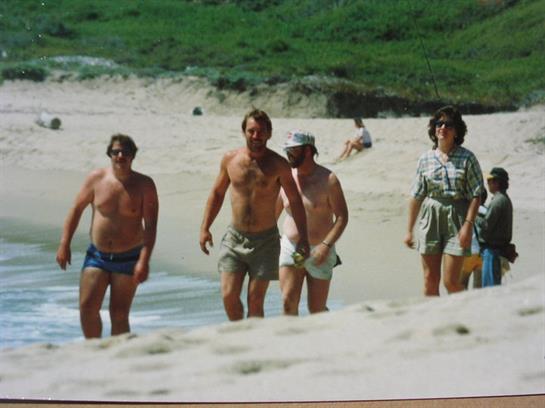 Five friends walk on a sunny beach, savoring each other's company and the ocean breeze.