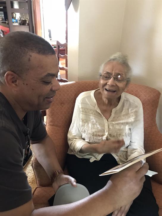 A man and an elderly woman laugh together while enjoying a friendly conversation in a warm setting.