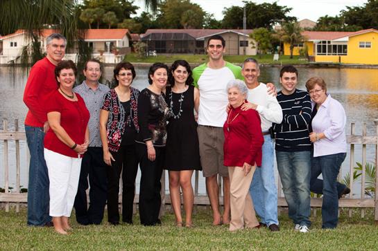 Family members stand together, smiling and chatting by the waterfront on a bright day.
