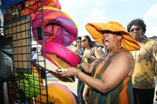 A woman surrounded by friends joyfully examines bright textiles at an outdoor market during daytime.