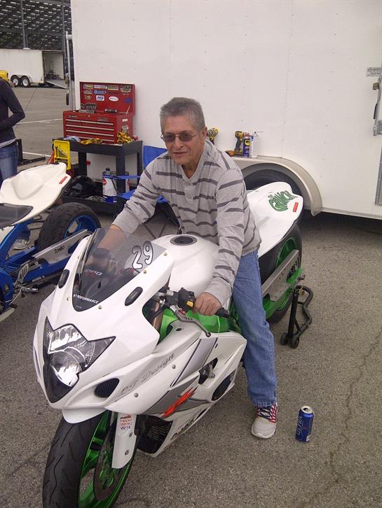 Man in sunglasses sits on a white sports bike in a tool-filled parking area.