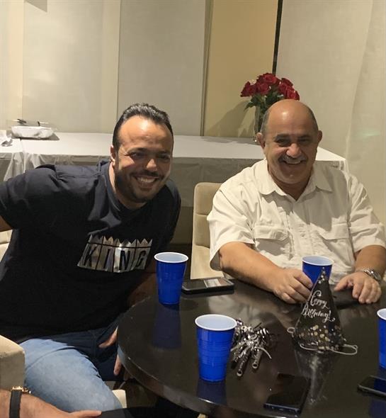 Two men are happily seated at a table, sharing drinks and laughter in a relaxed atmosphere.