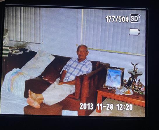 An elderly man enjoys a relaxed moment on a couch surrounded by family memorabilia and decor.