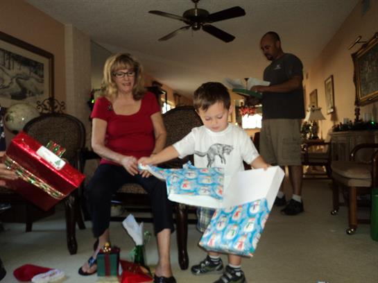 A young boy eagerly opens presents while family members enjoy the festive atmosphere.