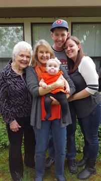 Four family members, spanning generations, gather outdoors with a smiling baby in their arms.