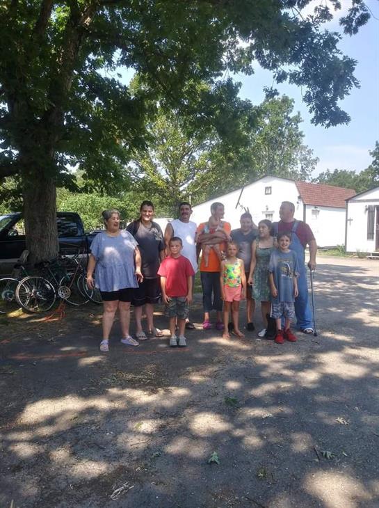 Group of adults and children stand together in the yard enjoying a sunny day near bicycles.