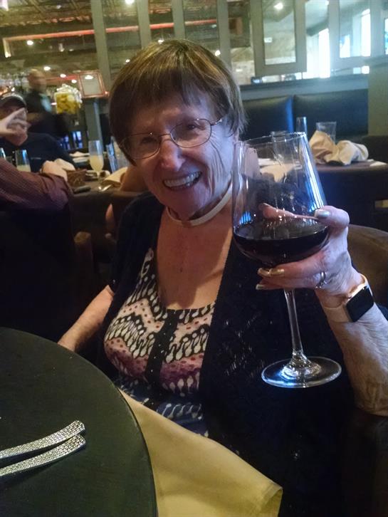 A joyful elderly woman holds up a glass of red wine, enjoying a meal with friends at a restaurant.