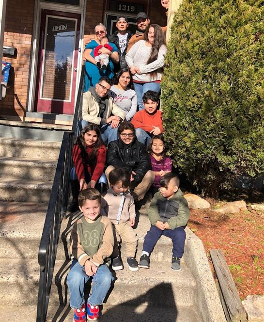 A large family poses together on the steps of their home on a sunny day in winter.