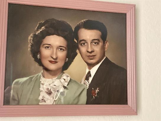A couple stands together in formal attire, exuding elegance from the mid-20th century.