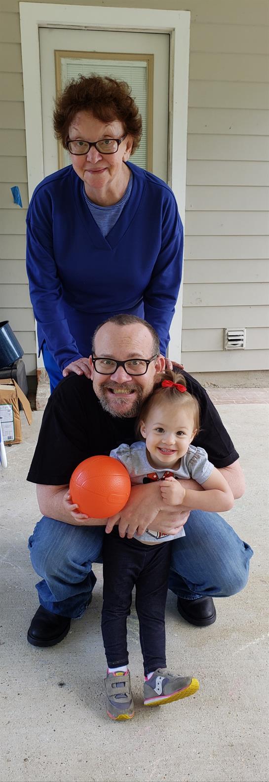 A father embraces his smiling daughter indoors while they play with an orange ball.