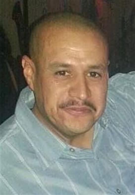 A man with a mustache smiles warmly while surrounded by friends, relaxing in a cozy environment.