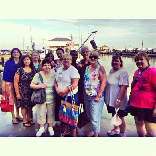 A cheerful group of women stands together at the marina, enjoying a sunny afternoon by the water.