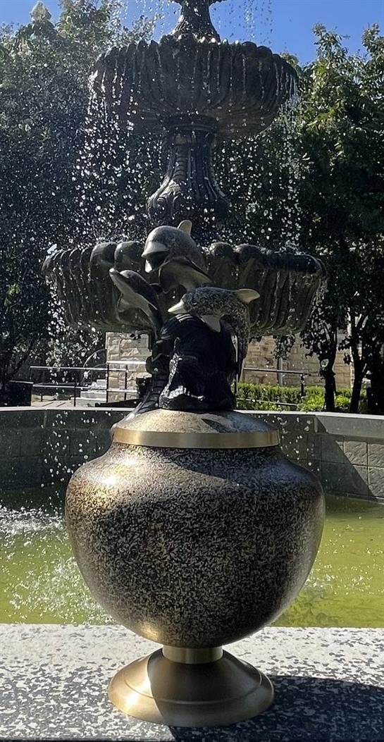 A stunning fountain features fish and human sculptures, splashing water in a peaceful park.