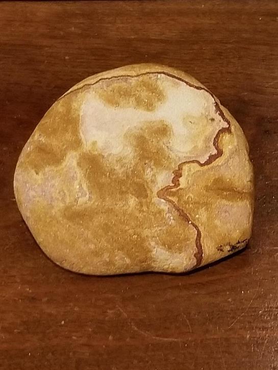 A smooth stone with intricate patterns resembling a human face rests on a wooden surface.