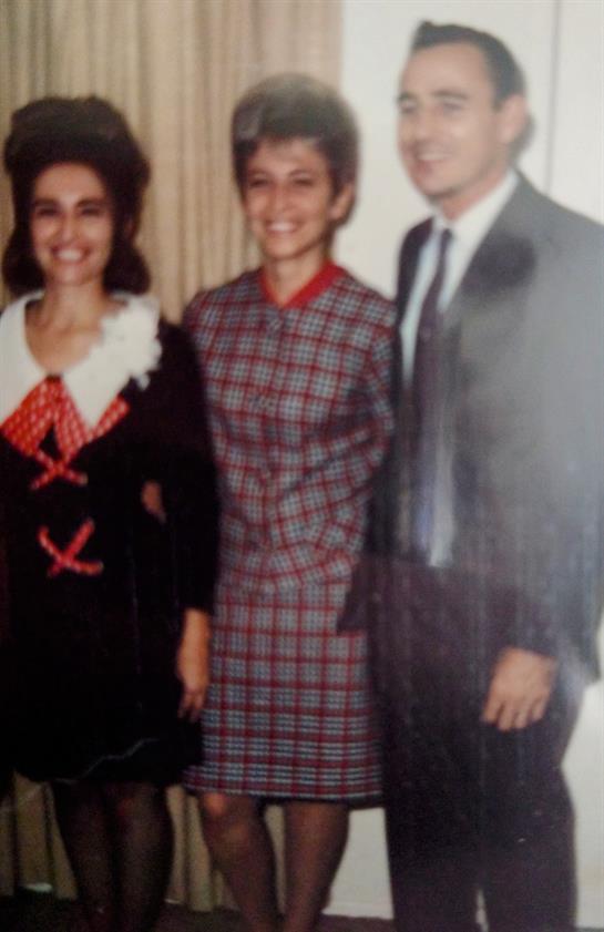 Three individuals are dressed in 1970s fashion, standing together, smiling at a social gathering.