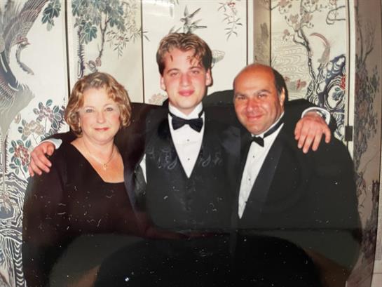 Three people pose together in formal wear, smiling warmly at a celebratory gathering.