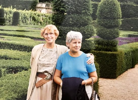 Two friends smile while exploring a beautifully manicured garden in the afternoon light.
