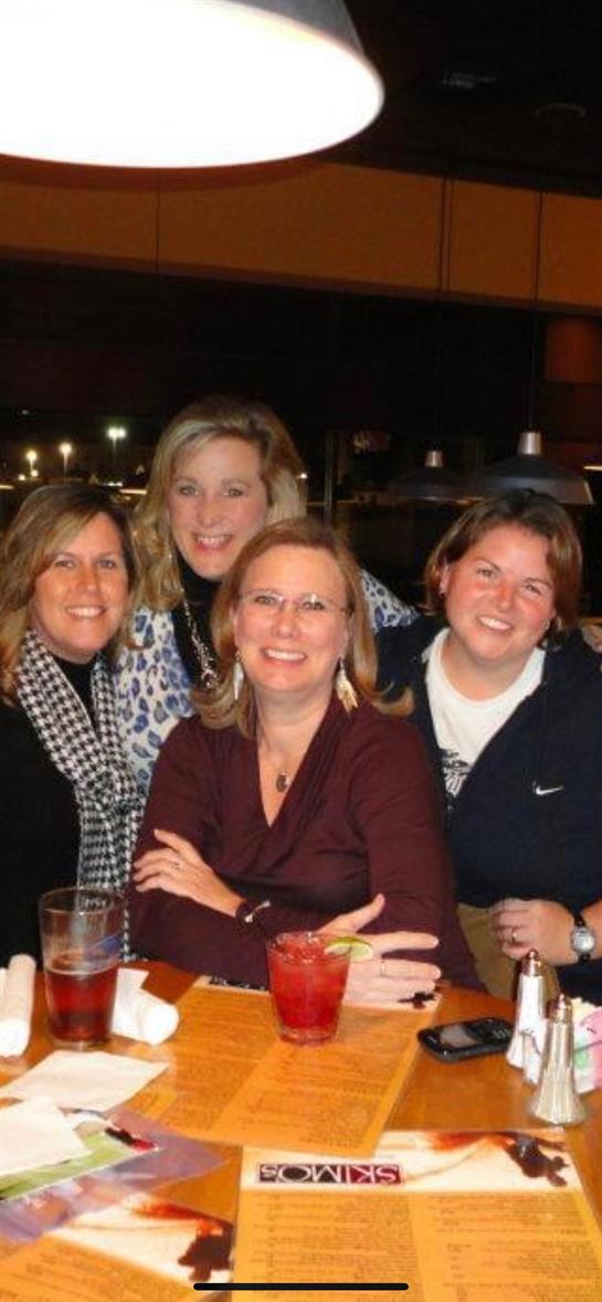 Four friends smile and pose together, enjoying drinks and conversation at a restaurant.