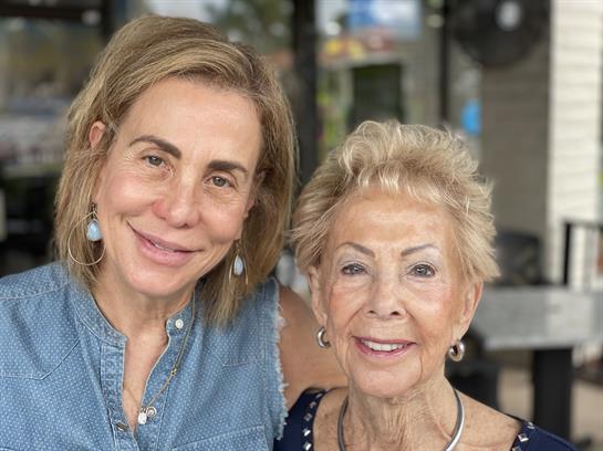 Two women enjoy a joyful moment in a cafe, sharing smiles and warmth under the afternoon sun.