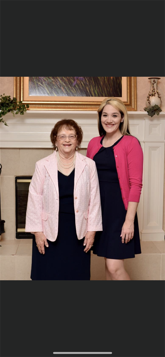 Two women share a joyful moment at a family gathering, dressed elegantly and smiling.