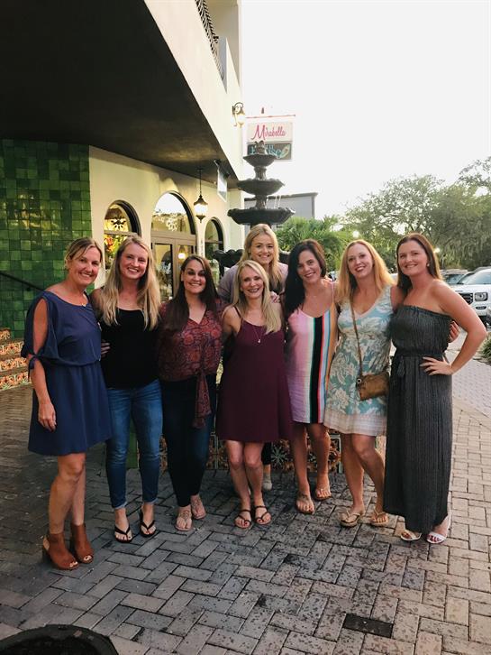 Nine friends gather for a cheerful moment outside a restaurant at dusk, capturing their smiles.