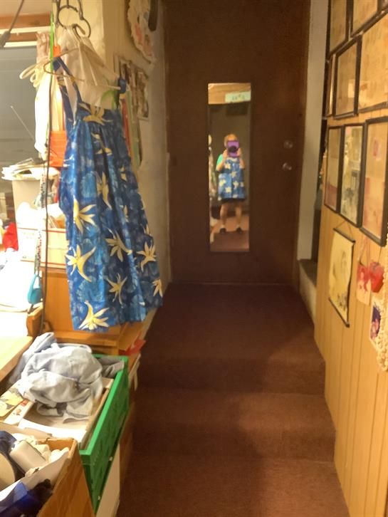 A vibrant blue dress displayed in a hallway filled with framed artworks and a mirror.