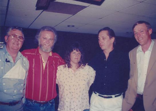 Friends stand closely together, smiling and enjoying a relaxed evening at a social event.