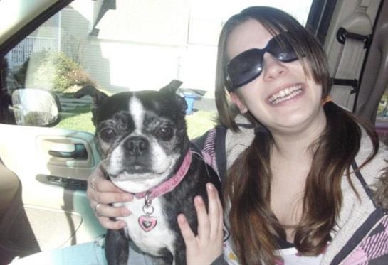 Girl with sunglasses smiles while holding her dog in the car on a sunny day.