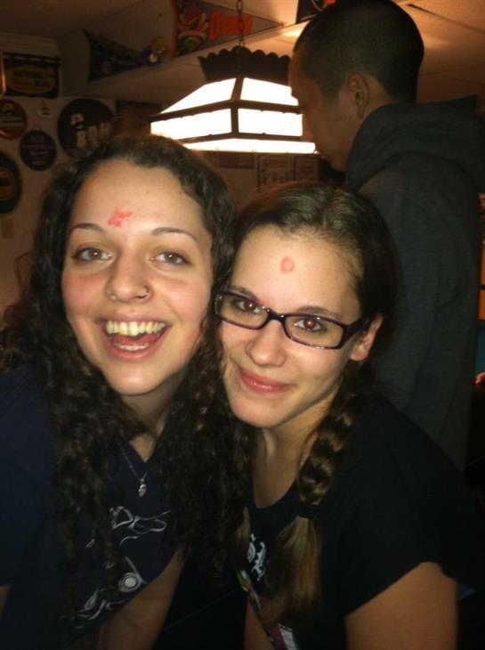 Two friends smile with playful red marks on their foreheads, celebrating together.