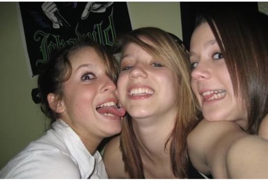 Three young women share laughter and playful antics at a cozy indoor gathering.