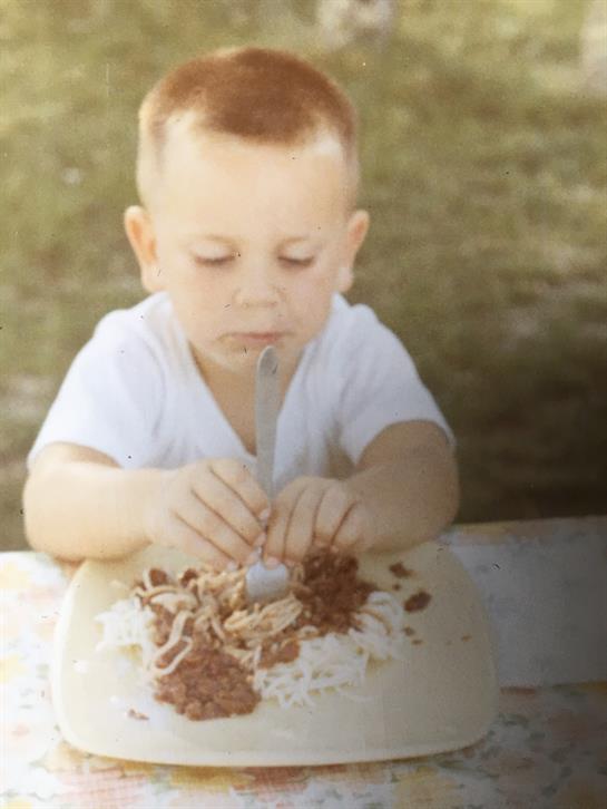 Young child enjoys manipulating food with a spoon in a grassy area while playing.
