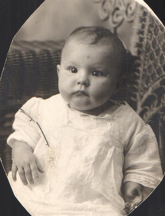 A baby dressed in vintage clothing poses indoors, reflecting a historical atmosphere and style.