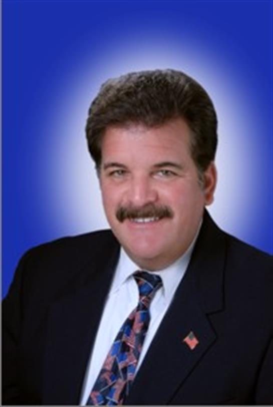 A businessman poses confidently in a suit with a friendly smile against a vibrant blue backdrop.