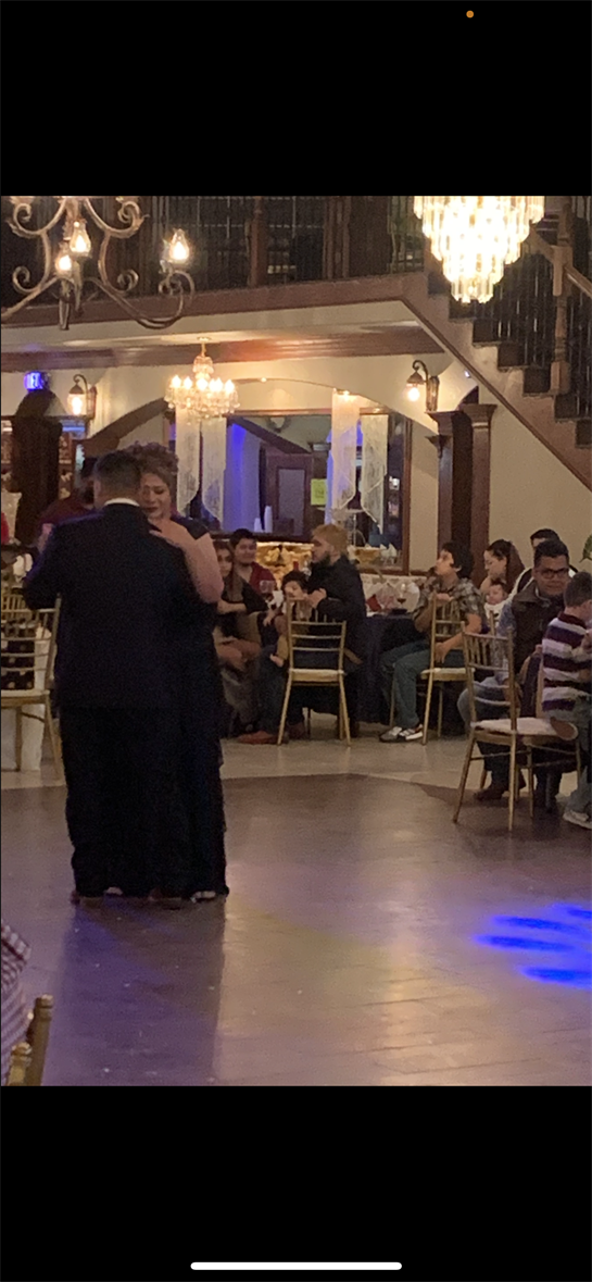Couple dances closely in formal wear at a wedding reception as guests enjoy the festivities.
