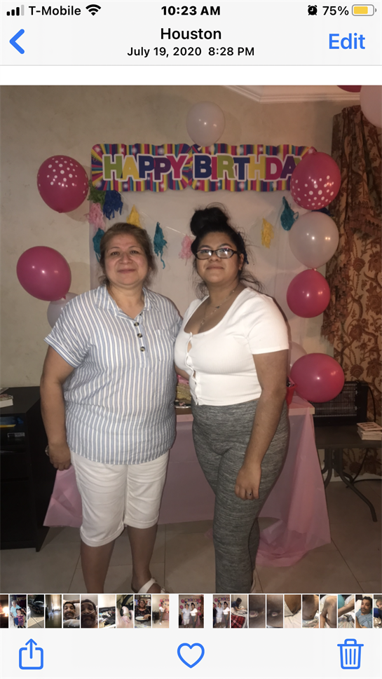 Two women smile in a decorated room celebrating a birthday with balloons and a banner.