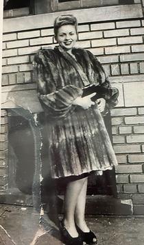 A woman in a fur coat stands confidently by a brick wall, highlighting vintage fashion.