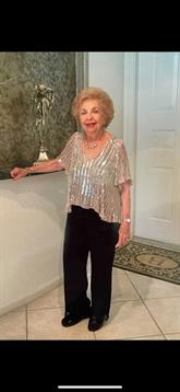 An elderly woman in a sparkly top and black pants stands confidently indoors.