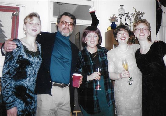 Group of five friends joyfully celebrating together in a warmly decorated room, sharing drinks.