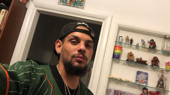 A man with a stylish appearance stands in a modern room showcasing various collectibles and decor.