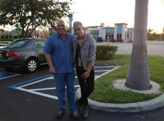 Two friends stand side by side in a parking lot. The sky shows signs of sunset with warm hues.