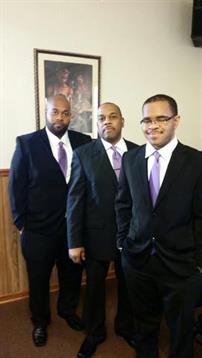 Three men dressed in formal suits with ties stand together in a modern indoor environment.