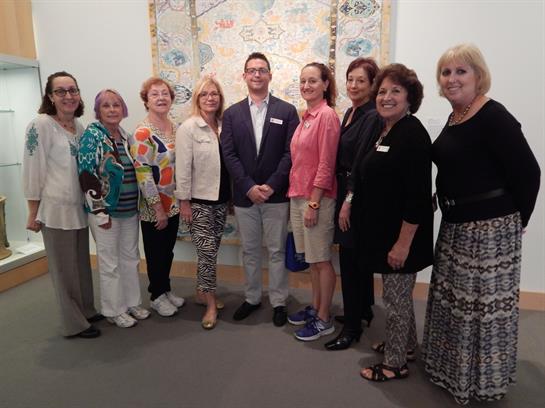 Women and a man gather for a group photo at an art exhibition featuring local artists.