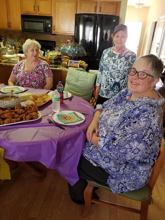 Three women enjoy their time at a gathering, sitting around a vibrant table filled with food.